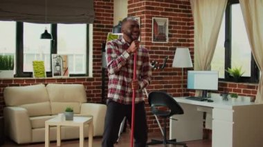 Happy male person dancing and washing floors with washing solution, using mop to sweep dust and dirt in apartment. Young man using cleaning tools to do housework and chores, singing.