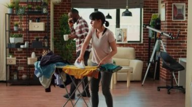 Angry girlfriend throwing shirt at boyfriend, being frustrated and ironing clothes at home. Young woman being stressed and trying to clean household, doing housework and chores.
