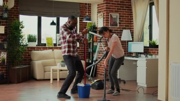 Diverse Couple Showing Dance Moves Having Fun Cleaning Apartment Using — Vídeo de stock