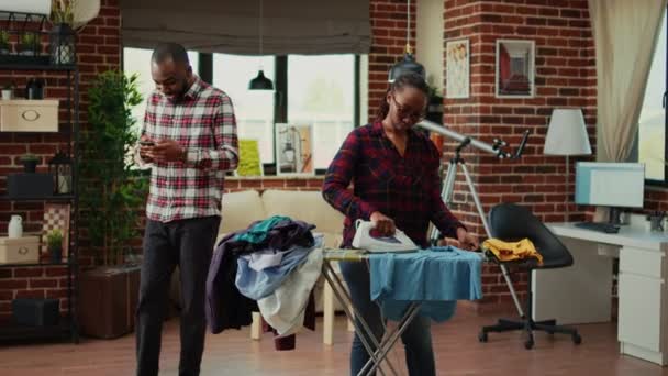 Stressed Young Person Ironing Laundered Apparel While Relaxed Husband Uses — Stock video