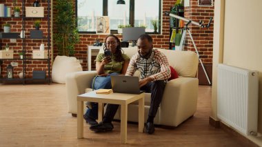 Afro-Amerikalı insanlar evlerinde kanepede dinleniyor, akıllı telefondaki sosyal medya uygulamalarına bakıyorlar. Boş zamanların, boş zamanların, eğlencenin, birlikte gülmenin, oturma odasındaki rahat eğlencenin tadını çıkarıyorum..