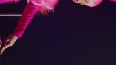 Vertical video: Asian performer with headphones playing techno music at turntables, standing at dj table having fun with fans at night in club. Musician performing techno music in studio over pink