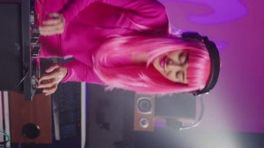 Vertical video: Artist standing at dj table mixing sound using mixer console, playing techno remix for fans during eletronic concert. Asian musician performing new album, enjoying having fun in club