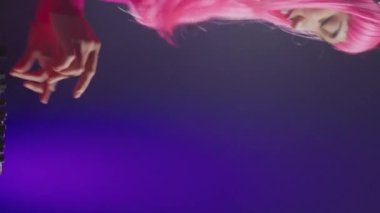 Vertical video: Asian performer mixing electronic sound using mixer console, dancing and having fun in club with fans during performance. Dj artist performing techno music using professional audio