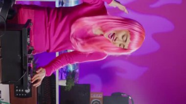 Vertical video: Artist creating musical performance with remix music using professional mixer console, having fun at night in club. Asian musician standing at dj table performing electronic song