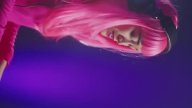 Vertical video: Dj in pink hair mixing electronic sound using mixer console, dancing and having fun in club with fans during performance. Asian artist performing techno music using professional audio