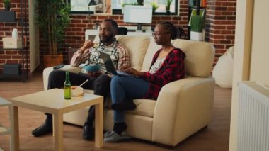 Young people watching movie together in living room, eating asian food with chopsticks and using online app on laptop. Happy couple having fun with favorite tv show, drinking alcohol.