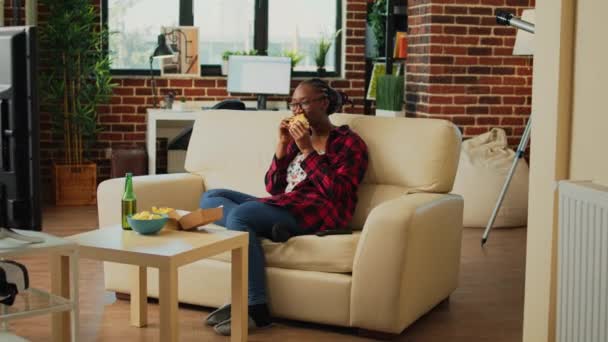 African American Person Taking Bite Burger Couch Eating Fast Food — Stockvideo