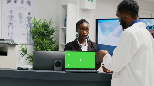 Medical specialists working at reception with greenscreen on laptop, using checkup form papers in health center. Isolated chroma key display with blank mockup template and copyspace on front desk.