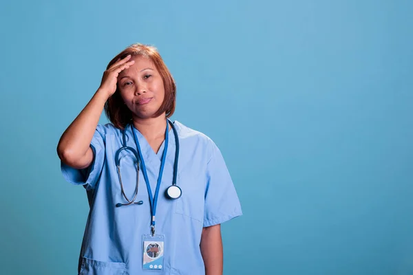 Elderly tired medical assistant suffering from headache after working at health care system expertise. Old depressed physician nurse having migraine during checkup visit appointment