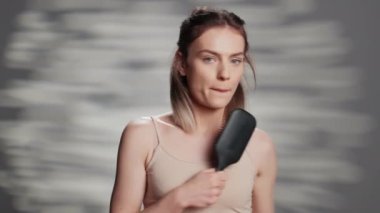 Positive confident person holding hair brush to sing, having fun in studio to advertise self acceptance and skincare ad campaign. Young woman with bare glowing skin promoting imperfections.