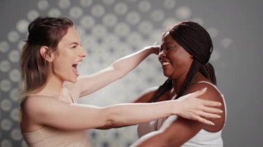 Cheerful gentle girls embracing imperfections on camera, posing together with self confidence. Interracial women with glowing skin feeling beautiful and unique in studio, advertising self love.