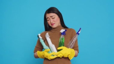 Overwhelmed tired housekeeper wearing gloves while holding multiple sanitary cleanliness products while cleaning house for clients. Stressed maid ensuring that everything was kept clean and organized.