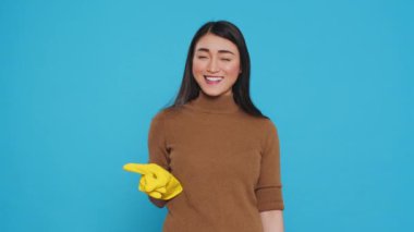 Professional housekepper pointing and showing cleaning advertisement or isolated text, standing on blue background in studio. Housewife worked hard to maintain a clean home, using hygiene products