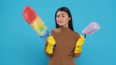 Asian housekeeper looking at professional both feather dusters trying to choose one before start cleaning house. Maid was known for her efficiency and her ability to get the job done quickly