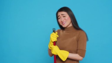 Happy housekepper dancing and having fun in studio while doing housecleaning using broom, dedicated to providing top-notch cleaning services to her clients. Housekeeping concept.