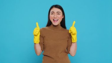Positive joyful maid smiling while doing ok gesture after finishing to clean client house, posing in studio over blue background. Cheerful housekeeper is responsible for providing cleaning services