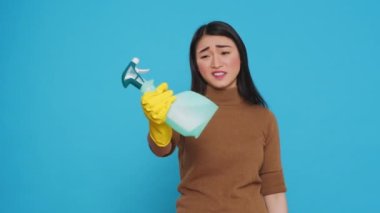 Upset house cleaner wearing yellow rubber gloves while showing chemical detergent spray in front of camera, explaining product efficient. Professional housekepper worked hard to maintain a clean home