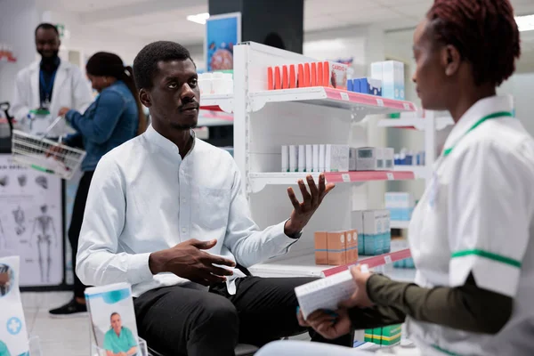 Pharmacist consultation, drugstore seller and customer talking, medic advising pills. African american man taking medicaments, chemist and client communication, all black team