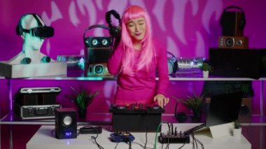 Smiling artist listening remix into headphones while mixing eletronic sound using professional mixer console. Performer standing at dj table dancing and having fun, enjoying party in night club