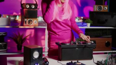 Asian artist using cutting-edge technology to remix music, listening song using headphones while performing in club at night time. Musician standing at dj table playing with professional mixer