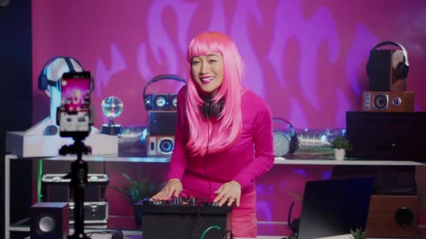 ミュージシャンは スマートフォンのカメラでミキシングプロセスを記録し プロのミキサーコンソールを使用してナイトクラブで電子音楽を演奏します テクノサウンドを演奏しながら ピンクの髪を持つDjアーティスト — ストック動画
