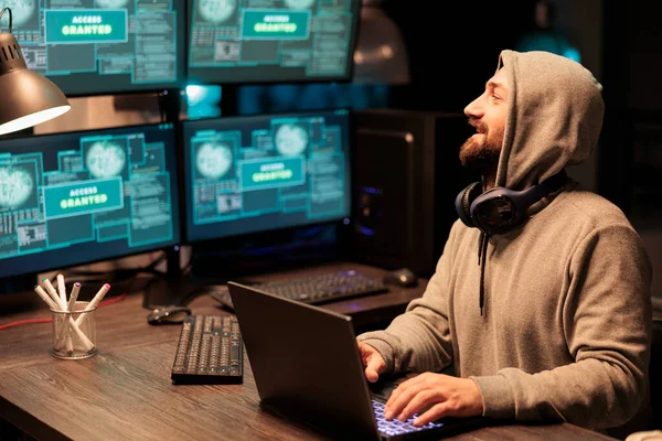 IT male hacker using computer to break system firewall, hacking security server. Dangerous thief breaking database and stealing information, working late at night with multiple monitors.
