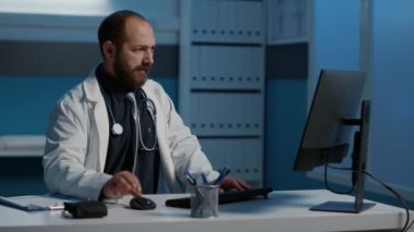 Gece geç saatlere kadar hastane ofisinde çalışan yorgun doktor hasta hastalık raporlarını analiz ediyor bilgisayar daktilo uzmanlığıyla ilgili. Stresli, tükenmiş planlama sağlık tedavisi