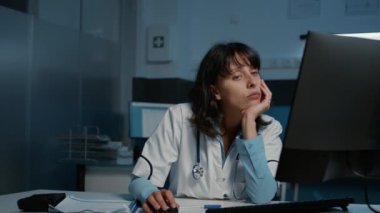 Exhausted stressed practitioner doctor working late at night in hospital office typing patient disease expertise while falling asleep on desk. Tired frustrated medic checking medical report on