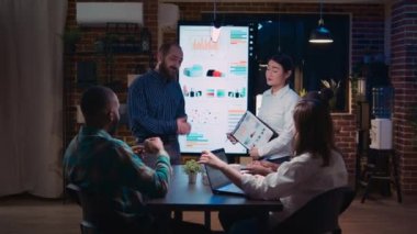 Diverse coworkers presenting company annual statistics report, employee planning marketing strategy in coworking space. Office workers in business meeting, revenue data presentation