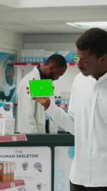 Vertical video: Young adult holding pack of drugs with greenscreen in pharmacy, showing isolated mockup template on pills boxes. Man using blank chromakey copyspace in healthcare retail shop.