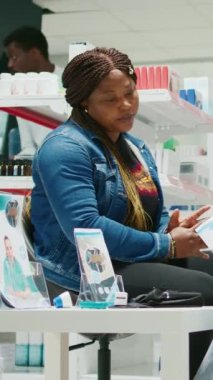 Vertical video: Young people checking boxes of medicaments, woman looking to buy vitamins and drugs in pharmacy shop. Pharmacist and customer asking about prescription treatment, pharmaceutics.