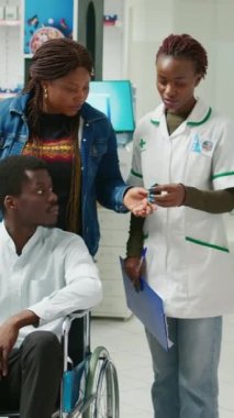 Vertical video: Female specialist giving drugs to wheelchair user, helping clients with healthcare products. Man with chronic disability and social worker buying vitamins and supplements from pharmacy