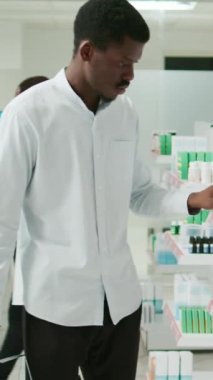 Vertical video: Male client checking boxes of vitamins on shelves, looking to buy pills and medical healthcare products. Person analyzing medicaments and drugs from pharmacy shop, drugstore service.