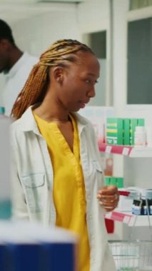 Vertical video: Female customer analyzing medical products in retail store, looking for pharmaceutics and healthcare drugs in pharmacy shop. Young woman checking packages of pills and medicine.