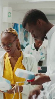 Vertical video: Man and woman looking for healthcare products in pharmacy, checking packages of medicaments and supplements. People buying prescription treatment or vitamins bottles. Tripod shot.