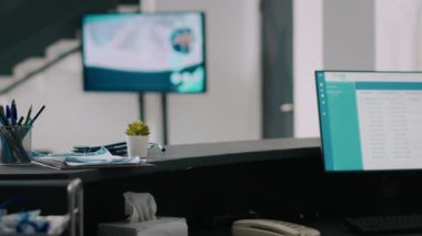 Hastanenin boş resepsiyonunda bilgisayar, hastalara bilgi ve randevu listesi gösteriliyor. Bekleme salonu lobisi, resepsiyonlu. Tıbbi muayeneleri ve raporları kontrol etmek için..