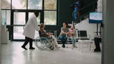 Old adult in wheelchair talking to young child in waiting area, family coming to visit senior patient with impairment. Wheelchair user trying to walk with walking frame in hospital lobby.