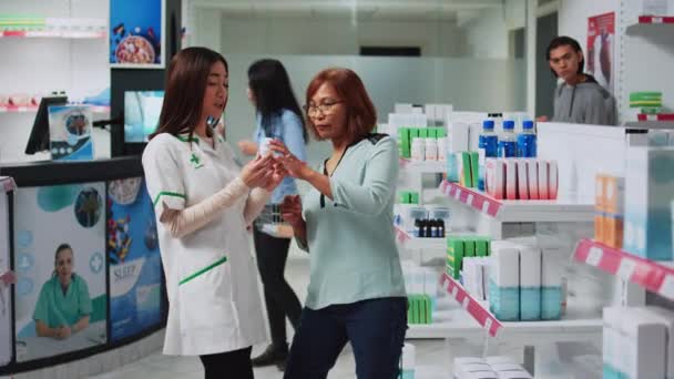 アジアの人々は 顧客と心臓病医学を分析します 薬剤師は 顧客に薬やサプリメントを与えます 保健医療のパッケージを見ている女性とドラッグストアの労働者 — ストック動画