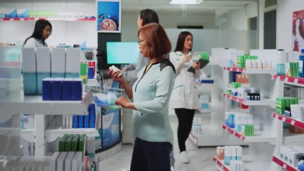 薬局のクライアントは 棚の上に心臓病薬の箱を読んで 医療医学を探しています 薬局で医薬品パッケージをチェックする女性の顧客 医療用品やビタミン — ストック動画