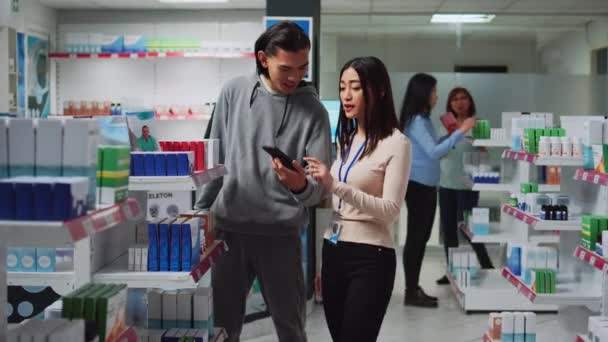 Kvinnliga Apotekare Tittar Smartphone För Att Piller Till Ung Man — Stockvideo