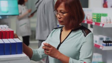 Tedavi için kardiyoloji hapı kutularına bakan bir kadın müşteri, eczaneye gidiyor. Kadın, ilaç paketlerini ve ilaç şişelerini hastalıkları tedavi etmek için kontrol ediyor. El kamerasıyla..