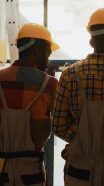 Dikey video: Lojistik ve envanter için barkodlu kutuları tarayan genç işçiler konteynır malzemeleri ile çalışıyorlar. Tarayıcı ve dijital tablet kullanan, mal paketlerini kontrol eden adamlar