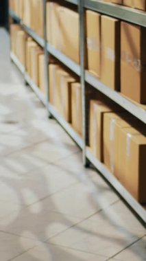 Dikey video: Ürün dağıtımı ve sevkiyatı için hazırlanmış raflarda, paketlerde ve karton kutuların bulunduğu depo malzemeleri. Perakende mağaza kargosuyla depo odası, endüstriyel