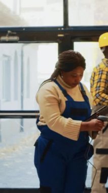 Dikey video: Depo çalışanı paketlerdeki barkodları tarıyor, raflardaki ve raflardaki ürünleri kontrol etmek için tarayıcı ve tabletle çalışıyor. Envanter için perakende mallarla çalışan genç bir kadın..