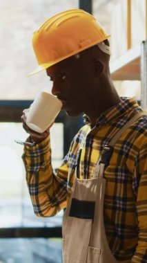 Dikey video: Erkek depo çalışanı karton kutulardaki eşyalarla dolu rafların yanında duruyor. Depoda perakende satış ürünleri ve ulaşım emriyle çalışan işçi.