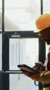 Dikey video: Depo çalışanı barkodları tarıyor, depoda stok yapmak için tarayıcı ve tablet kullanıyor. Depoda çalışan genç bir adam. Paketlerde mallar var..
