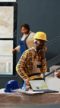 Dikey video: Genç erkek ve kadın ambalaj malzemeleri üzerinde çalışıyor, kağıt ve dizüstü bilgisayarla envanter planlamadan önce eğleniyorlar. İşçiler güler ve ürünleri karton kutulara koyar, kalite