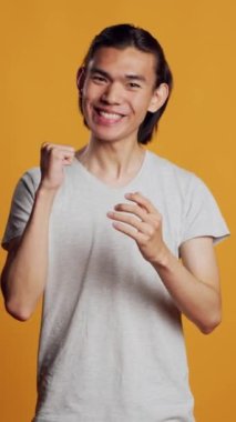 Dikey video: Asyalı adam kamerada el çırpıyor, gülümsüyor ve olumlu duygular gösteriyor. Neşeli kaygısız adam bir şey için alkışlıyor ve tezahürat yapıyor, tebrik ediyor. Ayakta alkışlama hareketi.