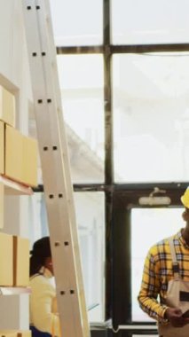 Vertical video: Team of men working on inventory order in warehouse, answering landline phone call to check products for transportation. Young empoyees doing teamwork to prepare merchandise stock.